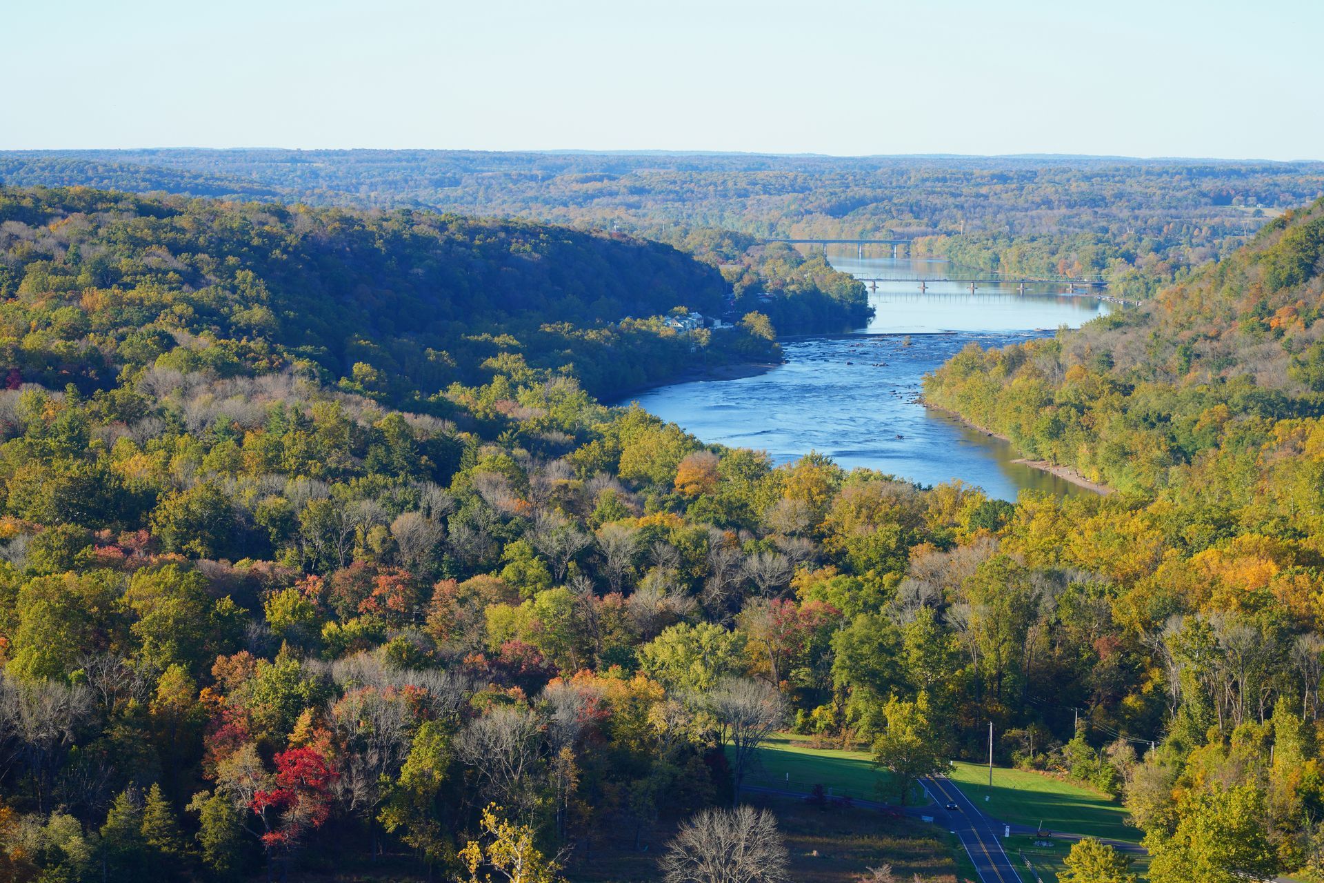 River flowing through a forest with autumn foliage. A bridge is in the distance.