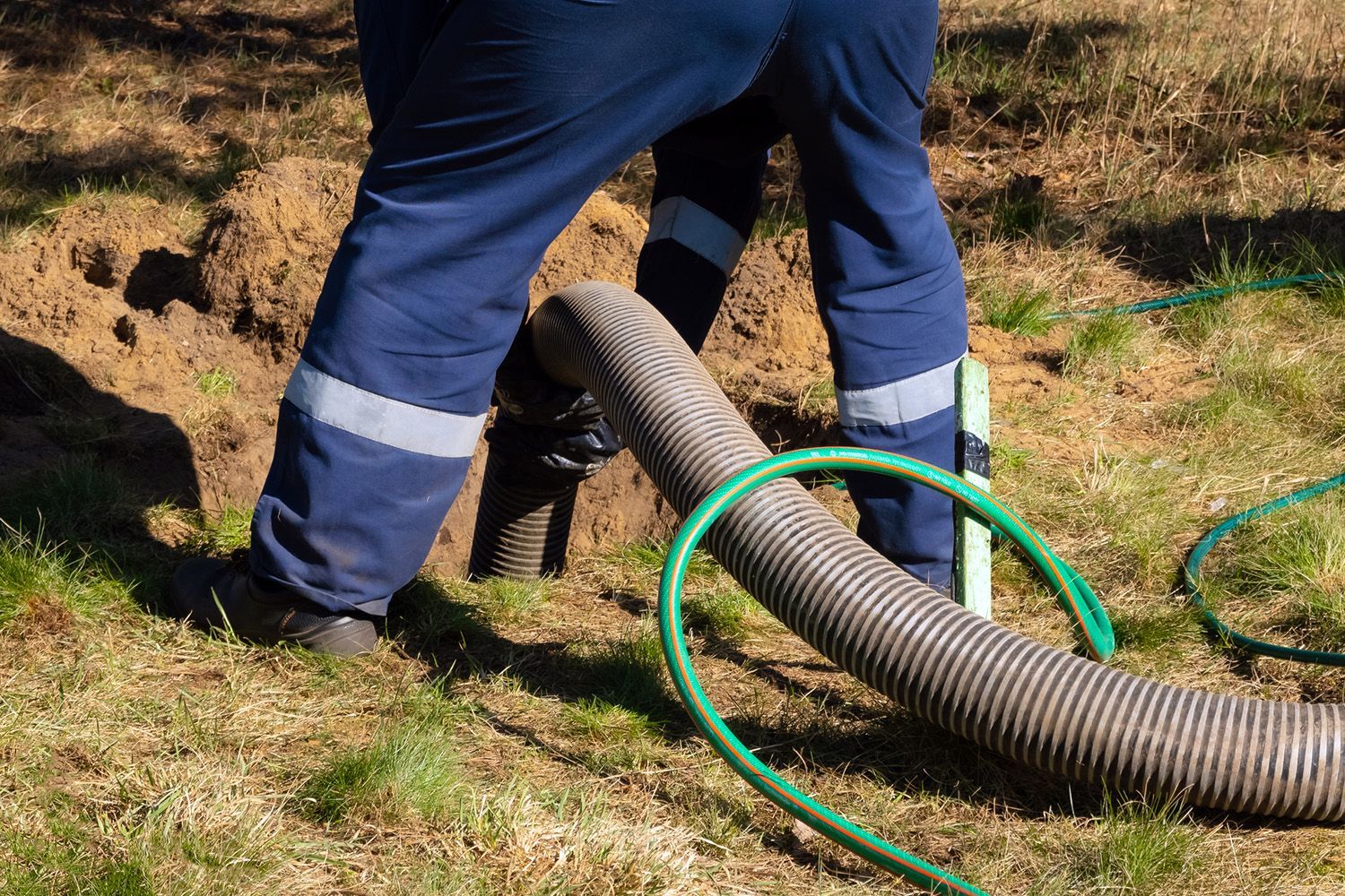 Person in blue work suit near a hole in the ground, with a hose extending from the hole.