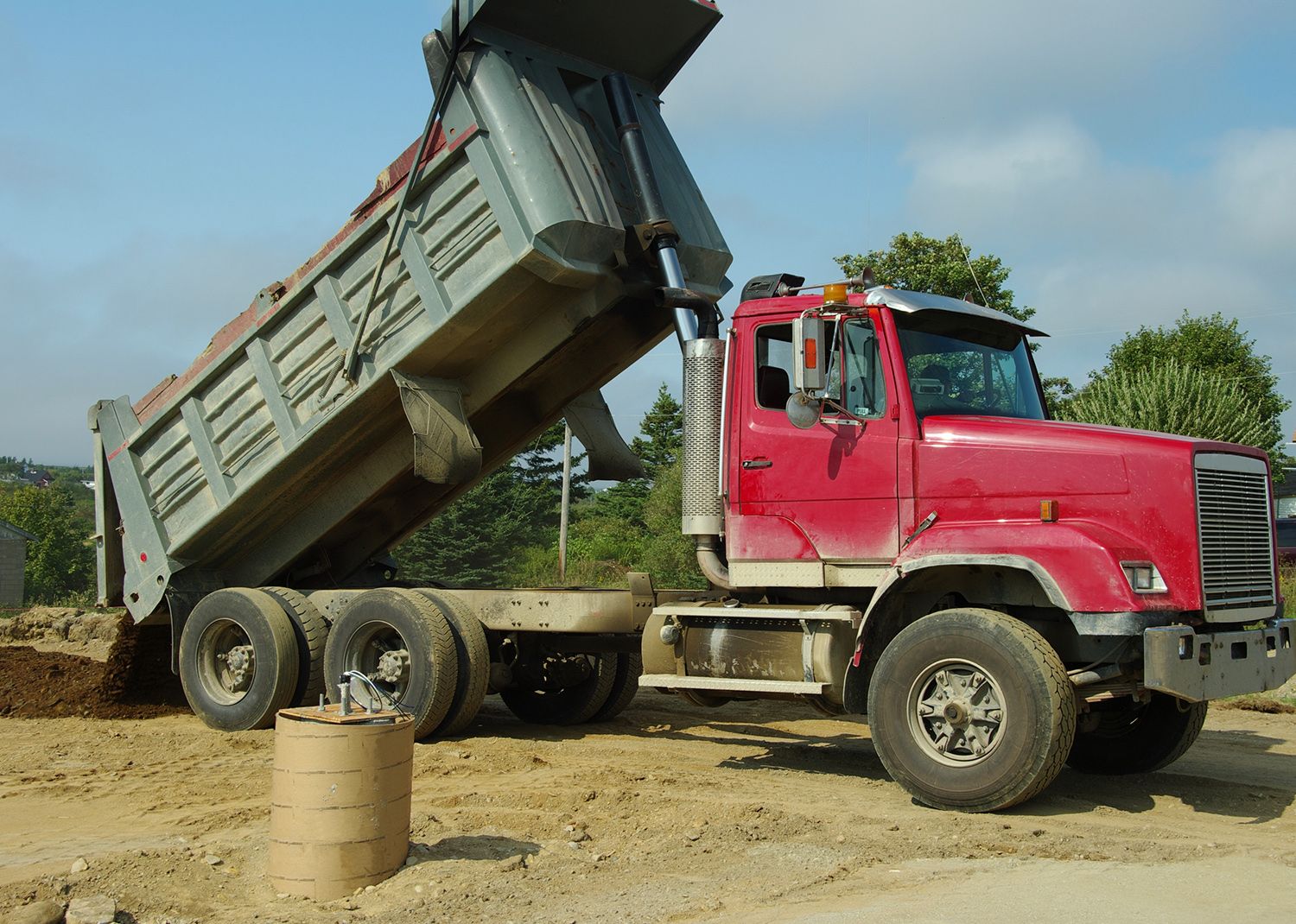 Red dump truck dumping dirt on a construction site; blue sky. Red dump truck dumping dirt on a construction site; blue sky.