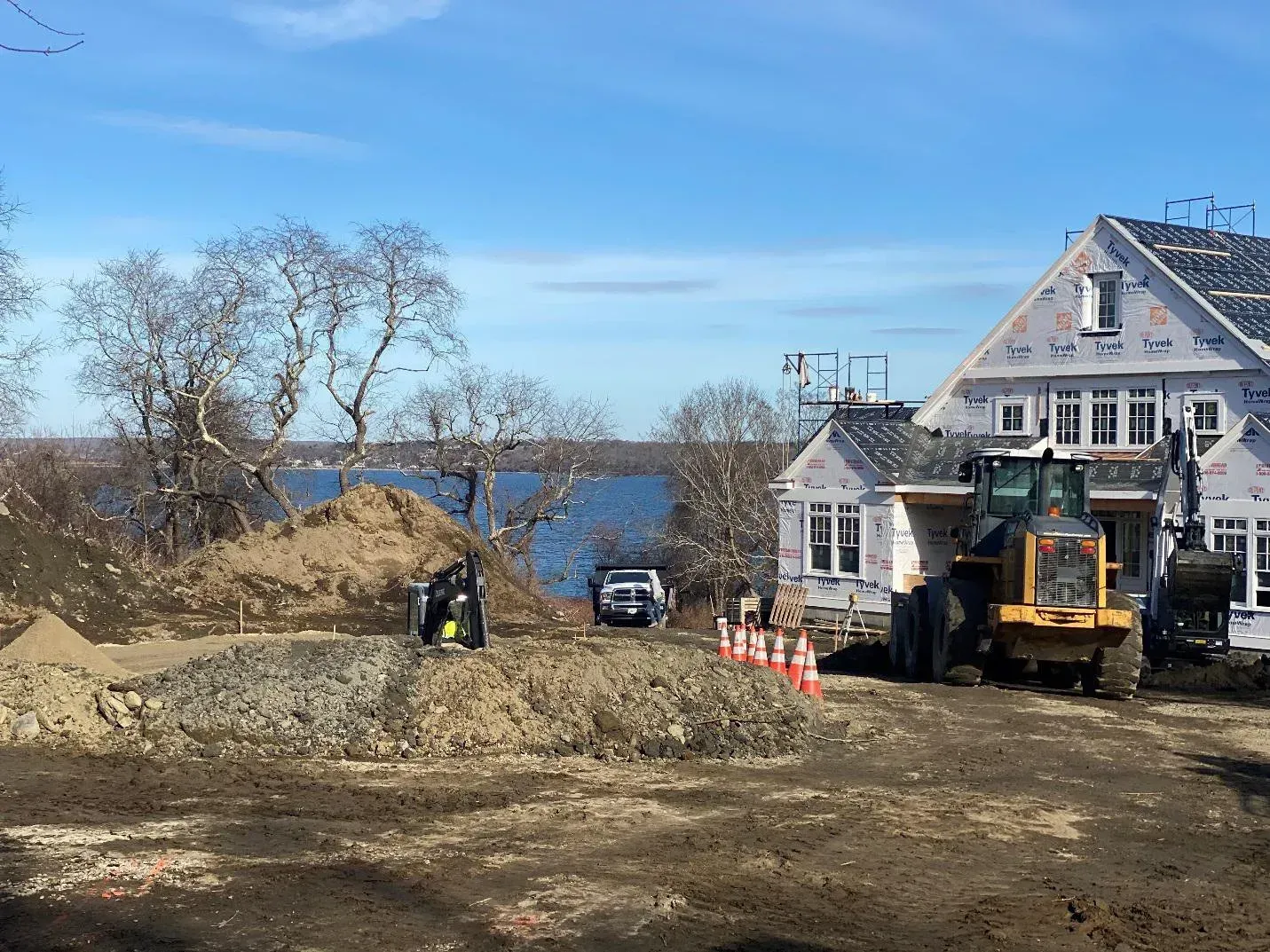 Construction site with building, earth moving equipment, and water view under blue sky.