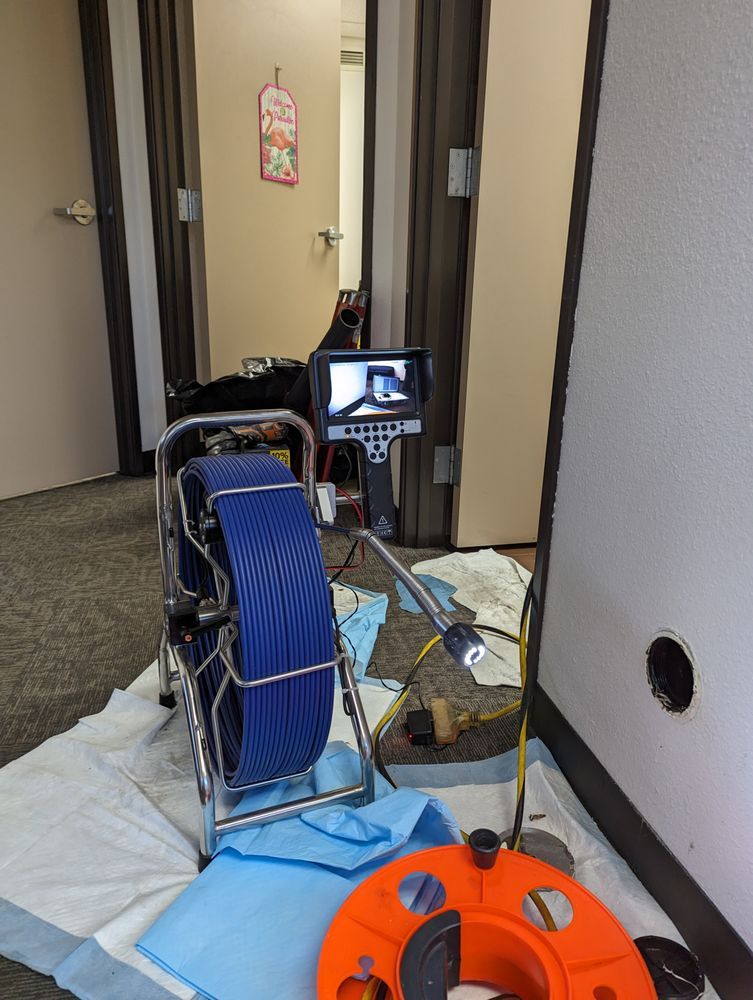 Plumbing inspection equipment set up in doorway, with blue cable reel and orange cable on floor.