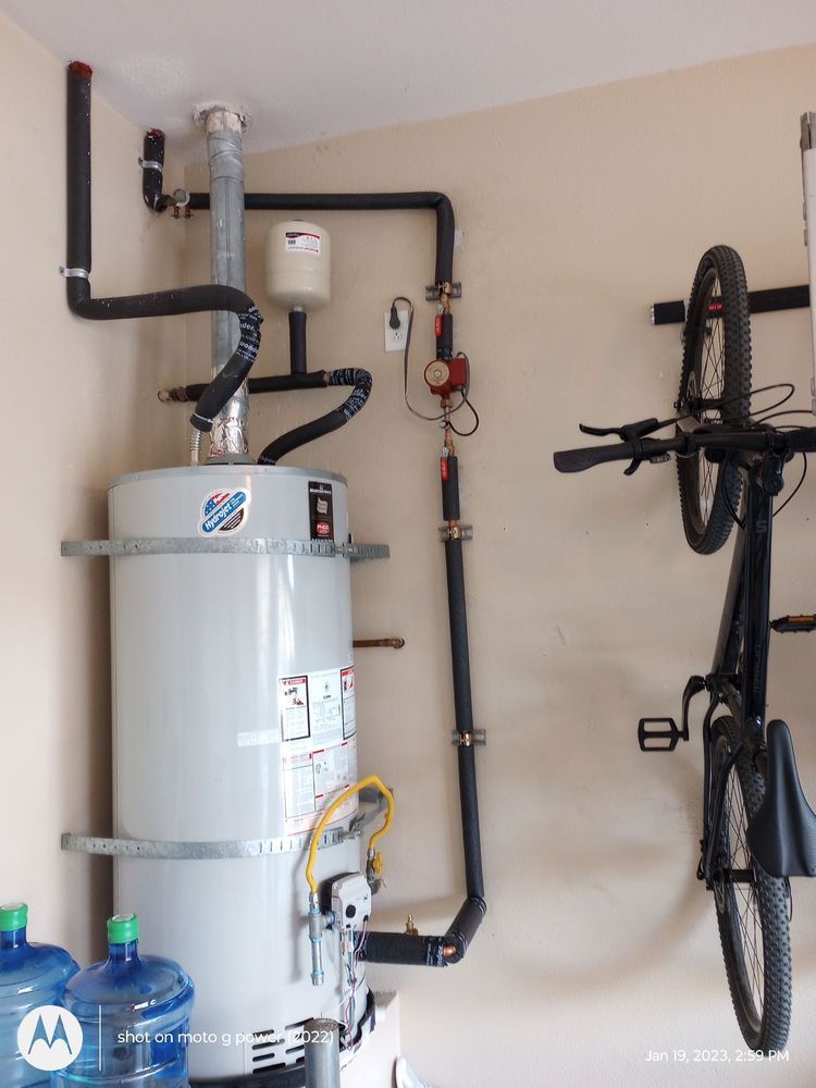 Water heater in garage with piping, a pressure relief valve, and a mounted bicycle.