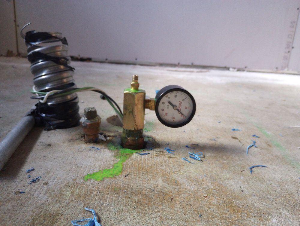 A pressure gauge with green liquid around its base on a concrete floor next to wrapped coils.