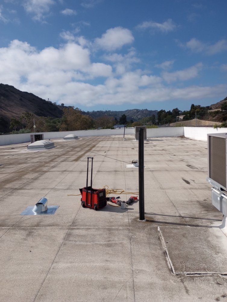 Flat roof with equipment, vents, and a scenic landscape under a blue sky with clouds.