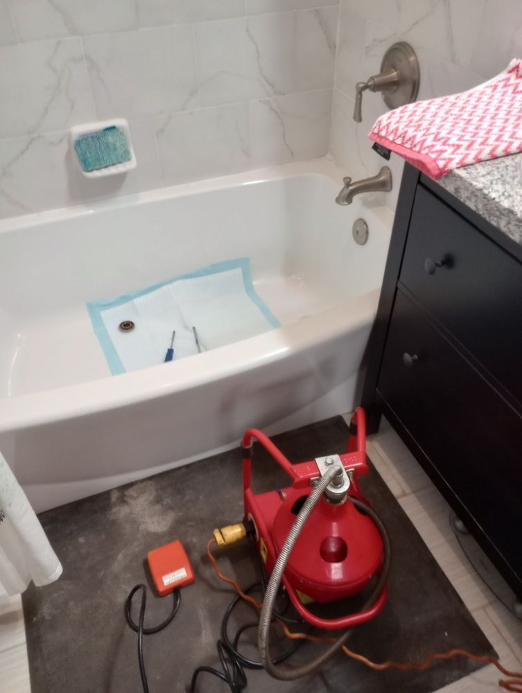 Bathroom with a red pump on the floor near the bathtub, suggesting a plumbing repair.
