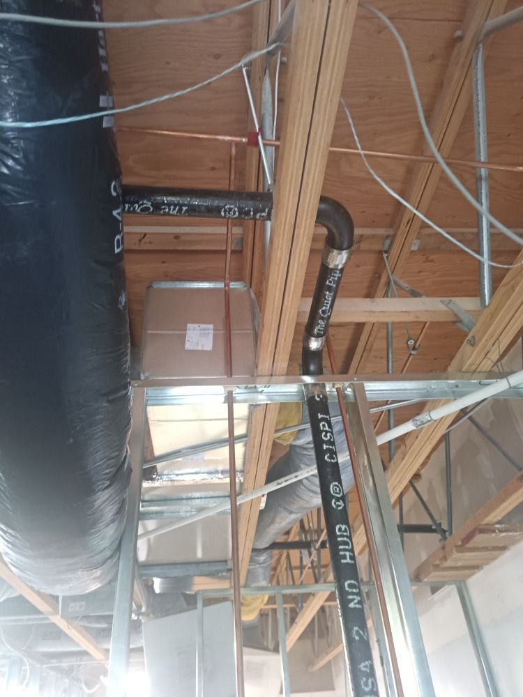 HVAC ductwork installation in a building's ceiling, with insulated black flex duct and rigid black pipe.