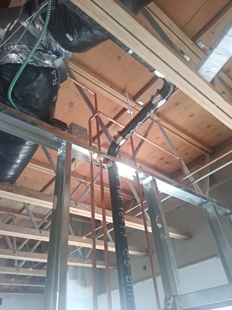 Plumbing pipes and ductwork installed in an unfinished interior, with metal framing and wood beams visible.