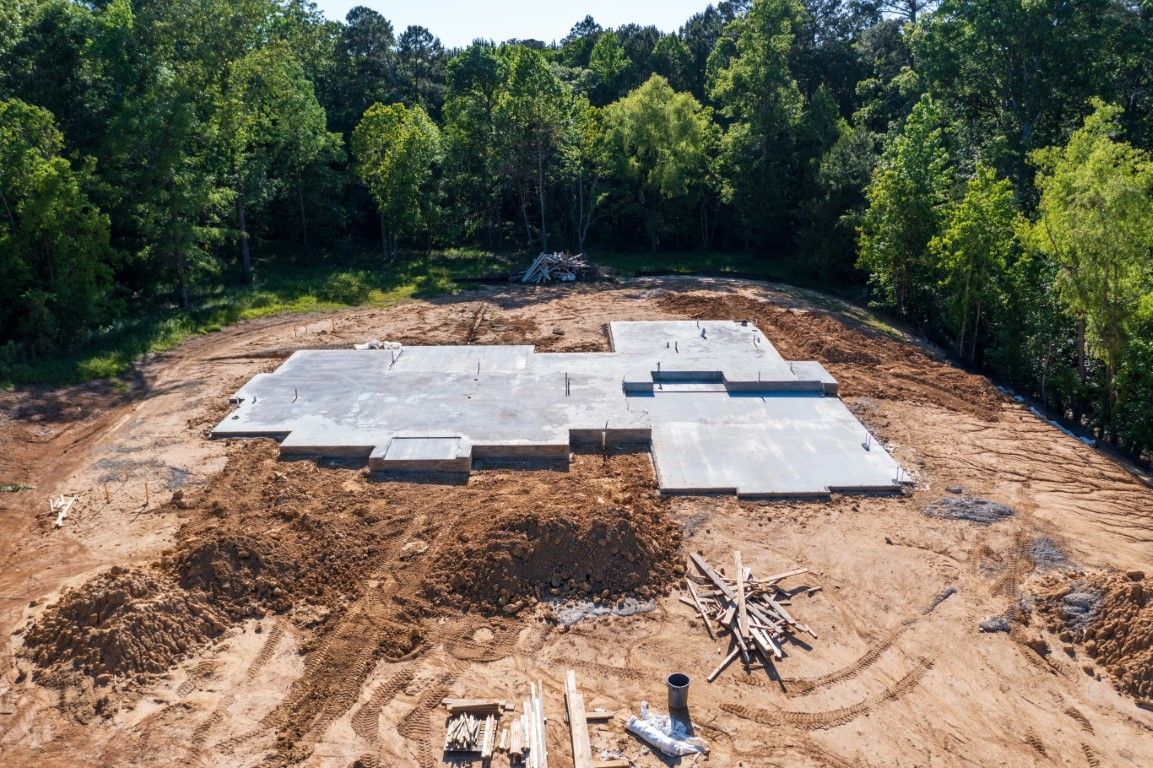 Concrete foundation for a house surrounded by dirt and trees, sunny day.