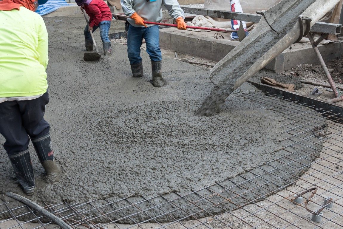 Construction workers pouring concrete on a foundation with rebar.
