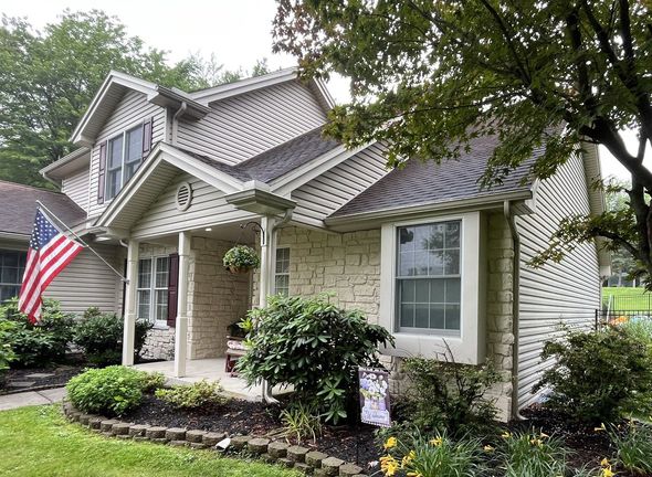 A two-story house with white siding, a shingled roof, a chimney, and a small front porch under a leafy tree.