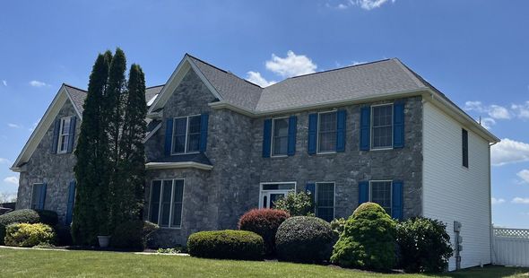 A two-story house with gray siding and stone veneer, with a blue service truck parked in the driveway on a sunny day.