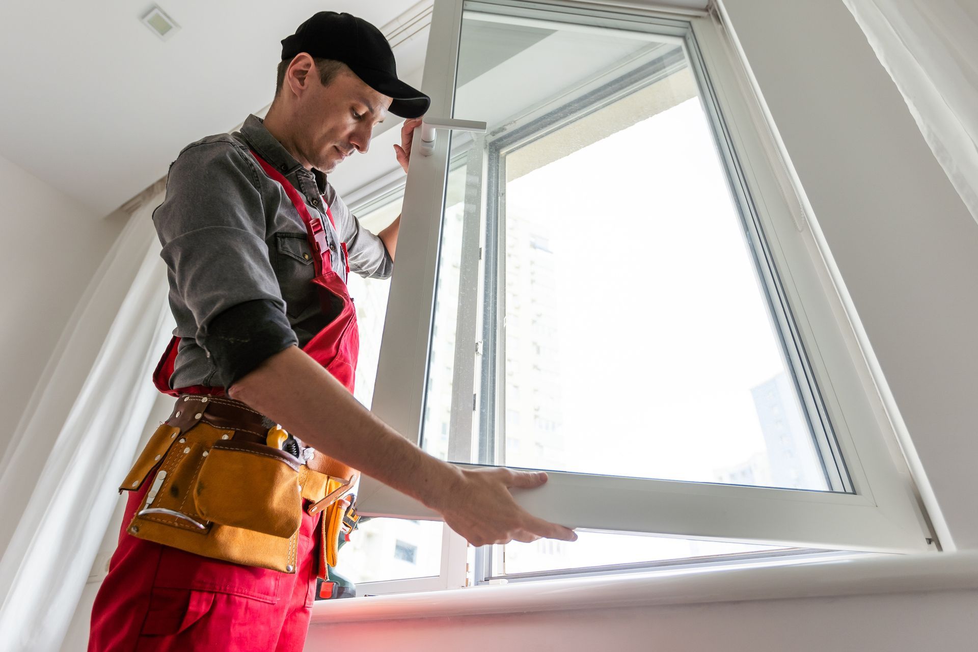 Uomo in abiti da lavoro che installa una finestra in una stanza luminosa.