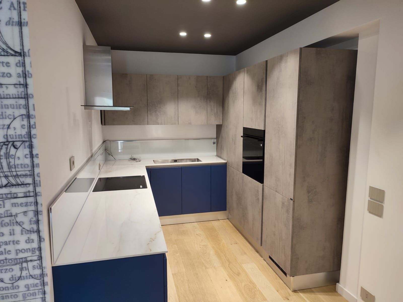 Cucina moderna con mobili grigi, mobili base blu e pavimenti in legno chiaro.