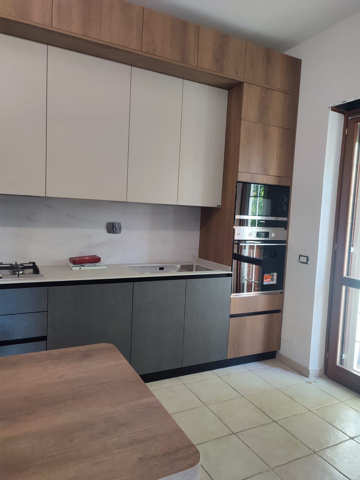 Cucina moderna con mobili grigi e bianchi, forno e dettagli in legno.