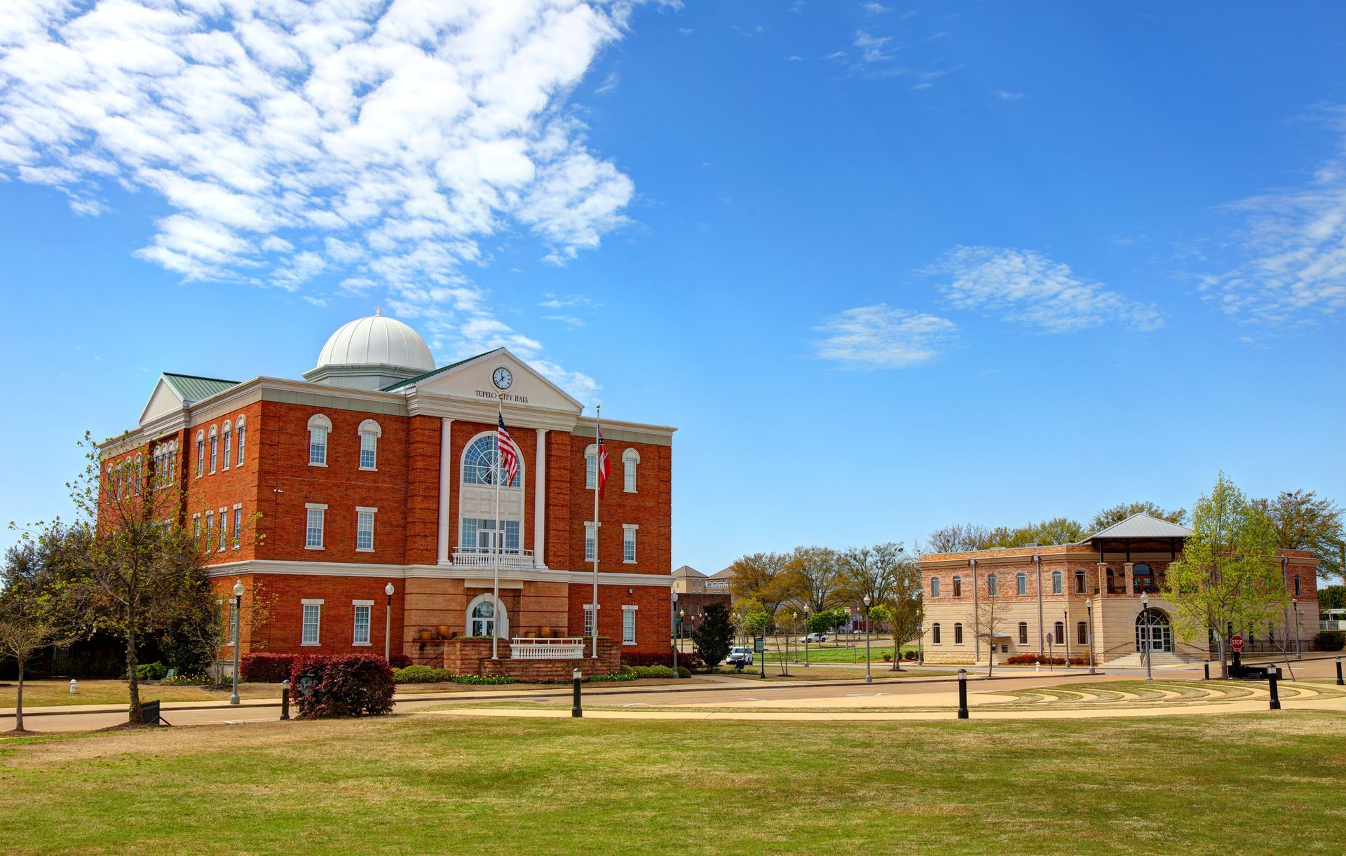 Brick buildings with white accents and a dome on a green lawn under a blue sky.