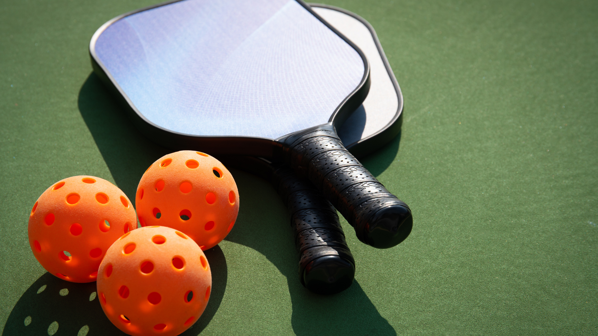 Two pickleball rackets and two orange balls on a green court.