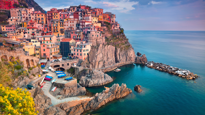 Colorful cliffside village overlooking a turquoise sea with a rocky harbor and breakwater