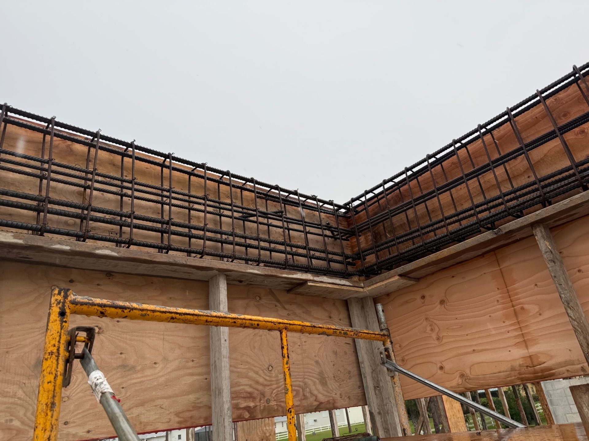 Construction site with workers on scaffolding beneath a partially built brick wall and roof framing