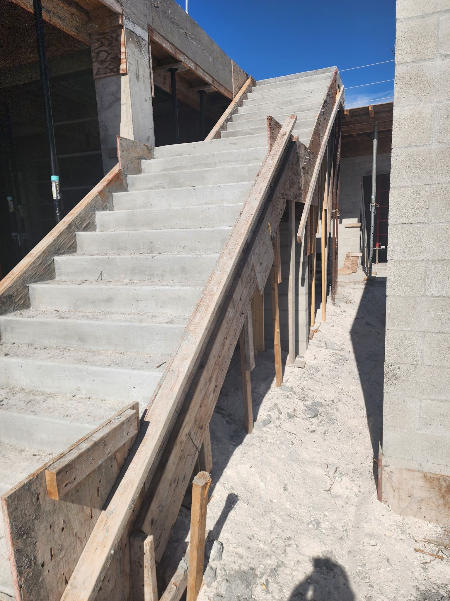 Concrete stairway under construction beside a sloped walkway, with wooden supports and unfinished walls.