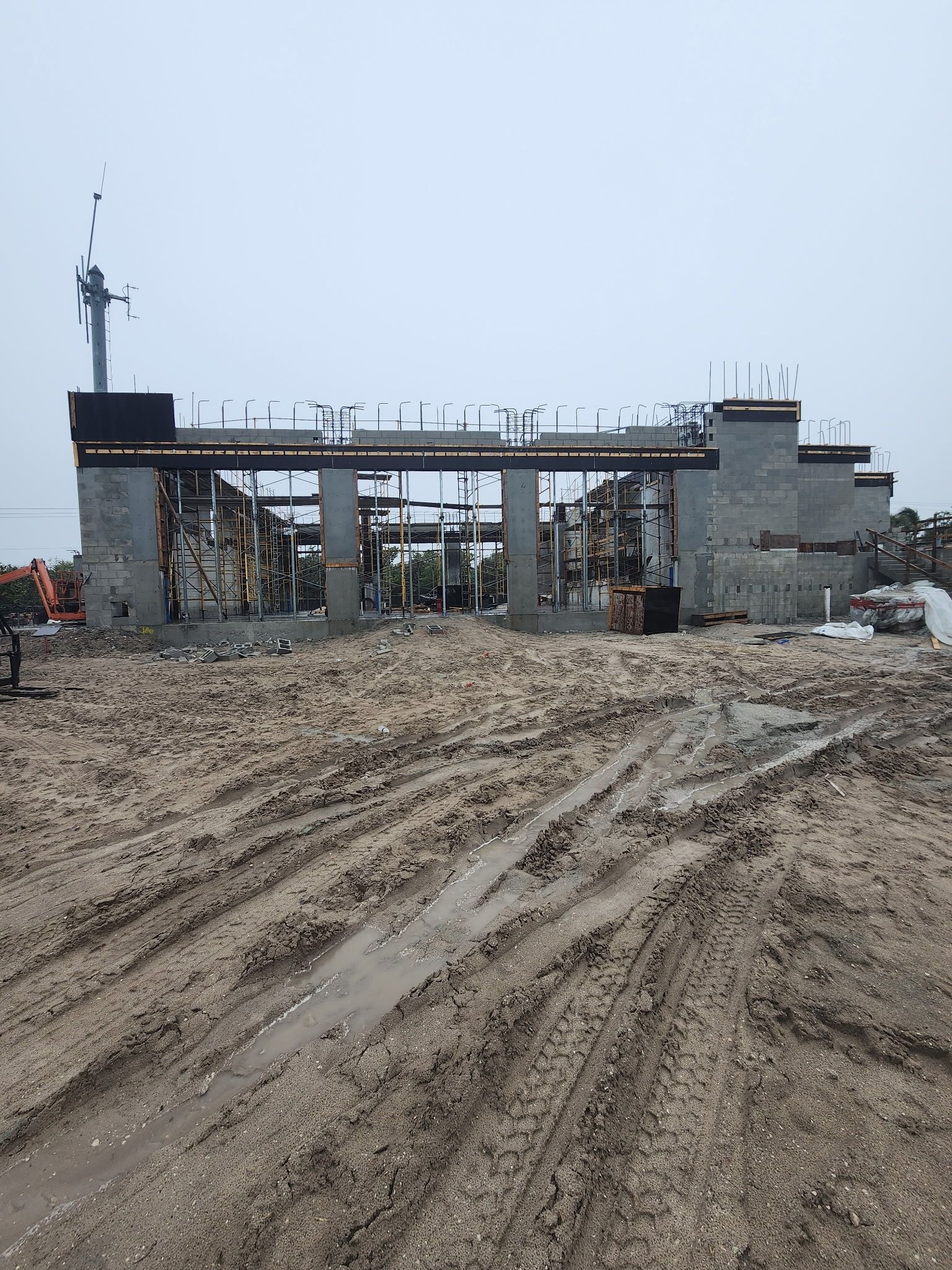Muddy construction site with an unfinished concrete structure and overcast sky
