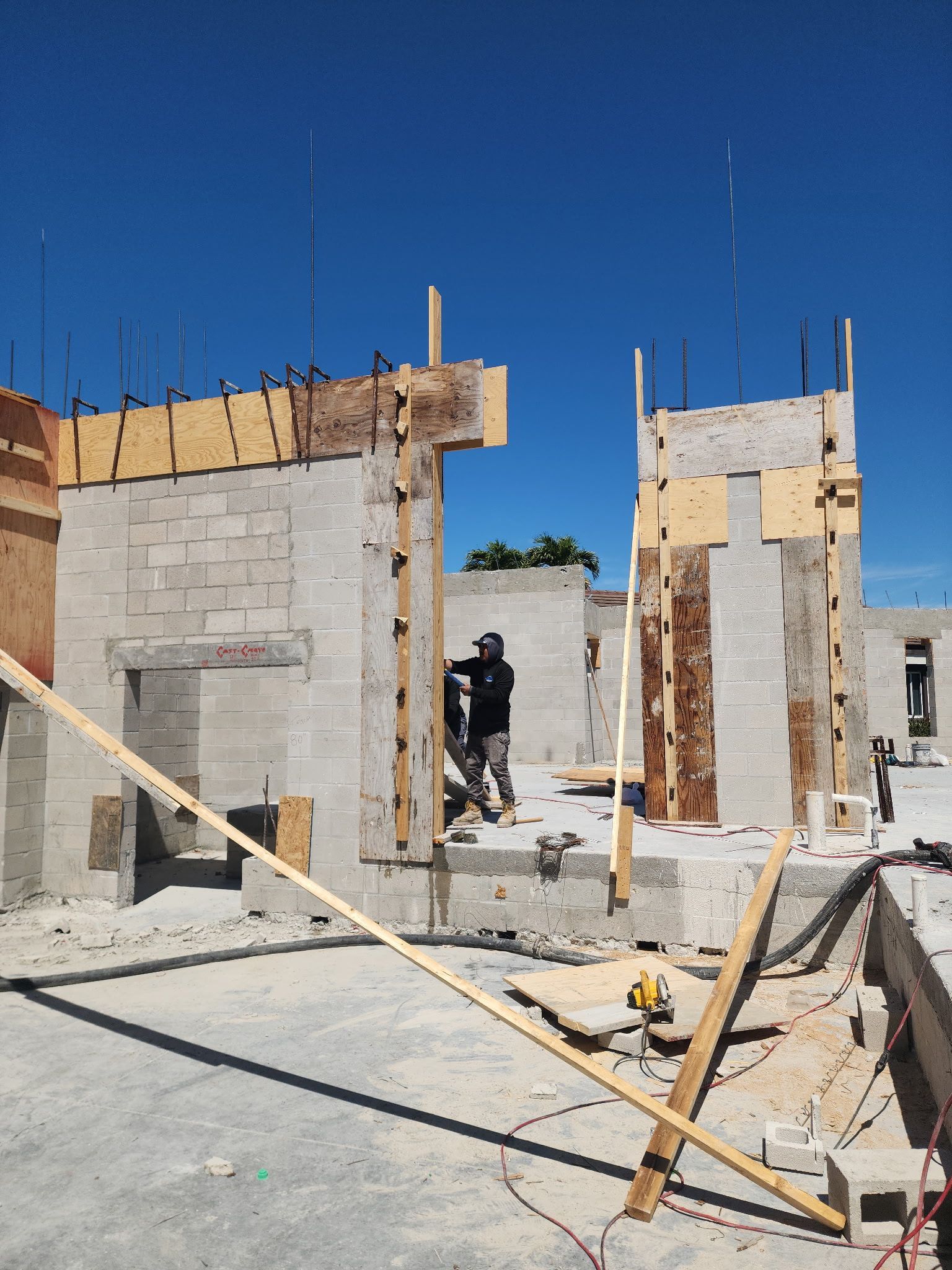 Construction site with unfinished concrete walls, wooden supports, and workers under a clear blue sky
