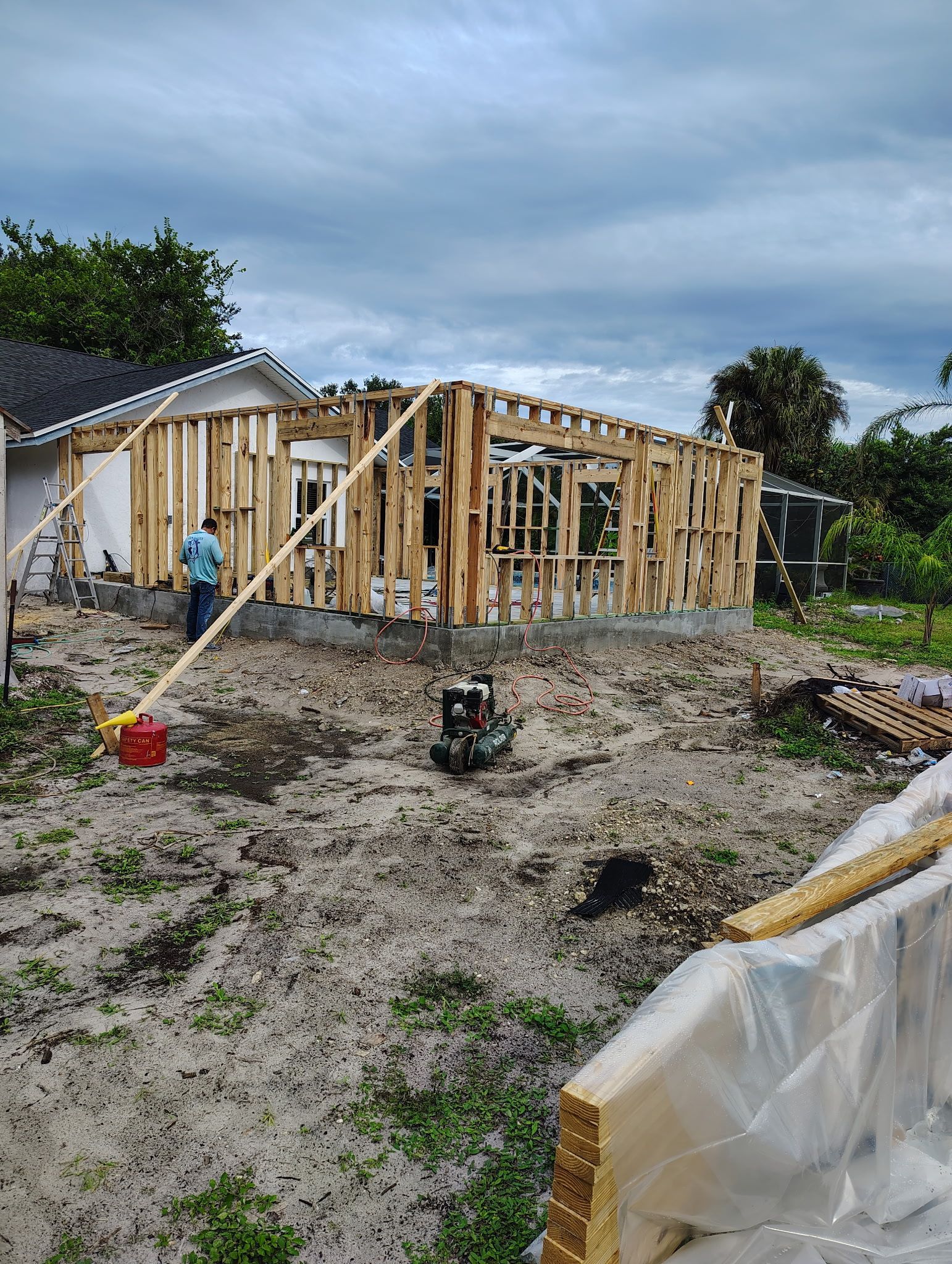 Construction site: wooden frame of a building in progress, person standing near it, cloudy sky.
