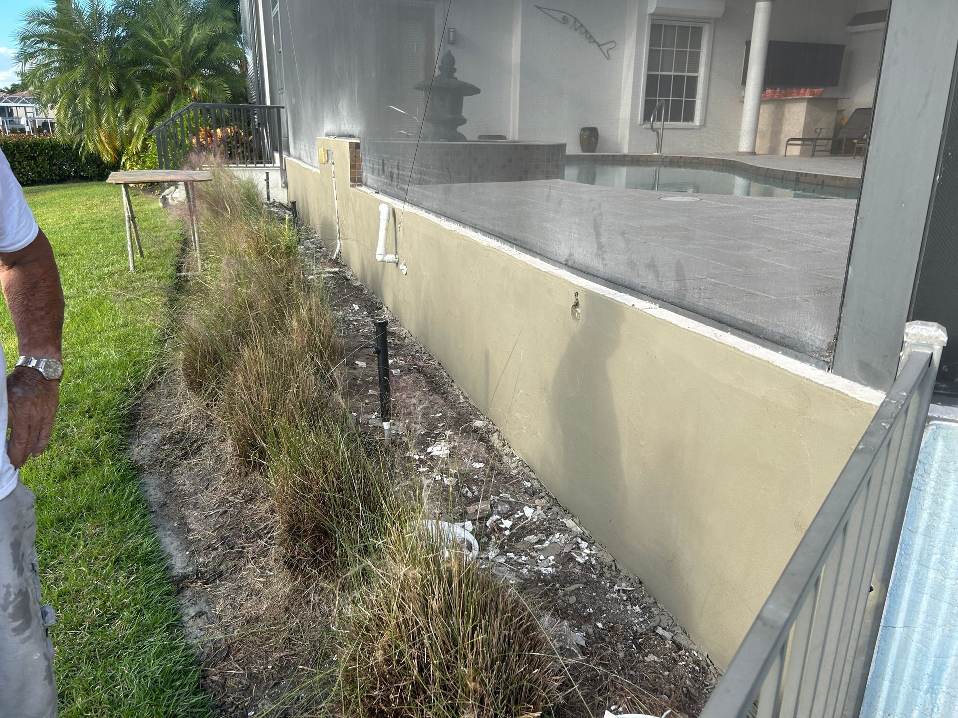 Person standing near a beige wall with dead plants. Pool and screened patio visible in the background.