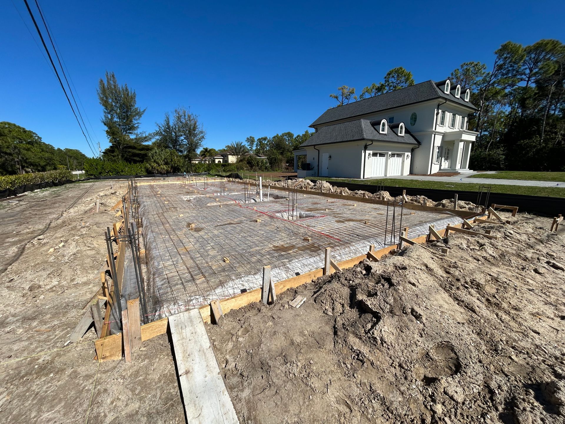 Concrete foundation slab under construction beside a white house on a sunny day