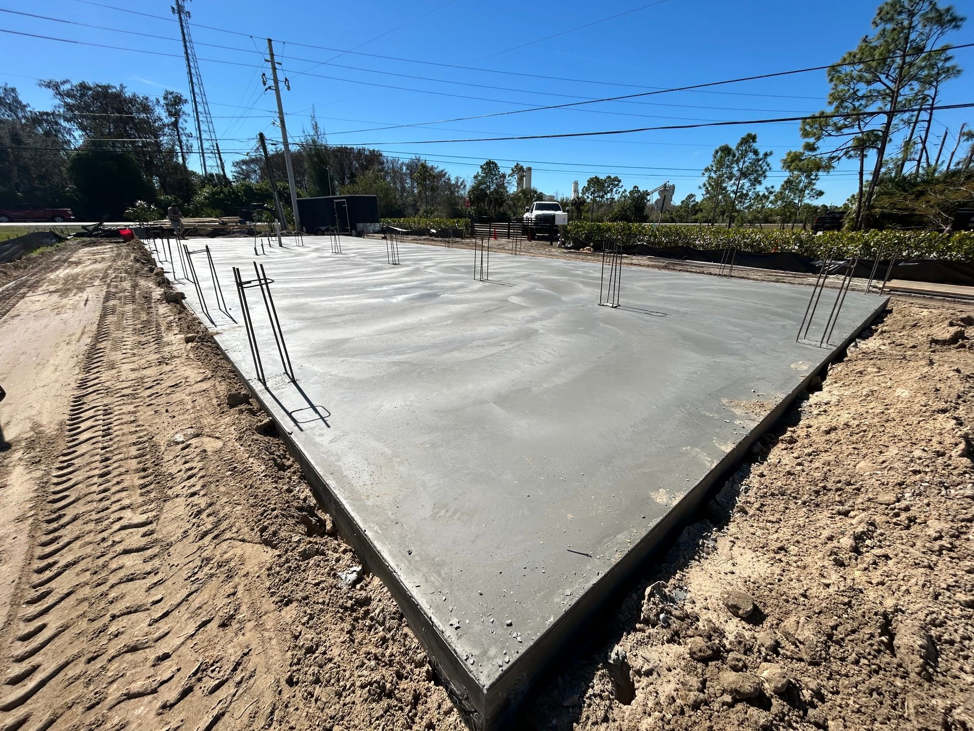 Fresh concrete foundation slab under construction with exposed rebar and dirt surrounding it