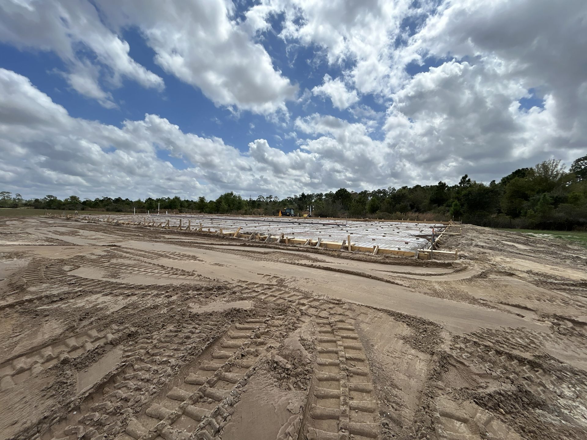 Mud construction site with tire tracks, shallow water, and cloudy blue sky