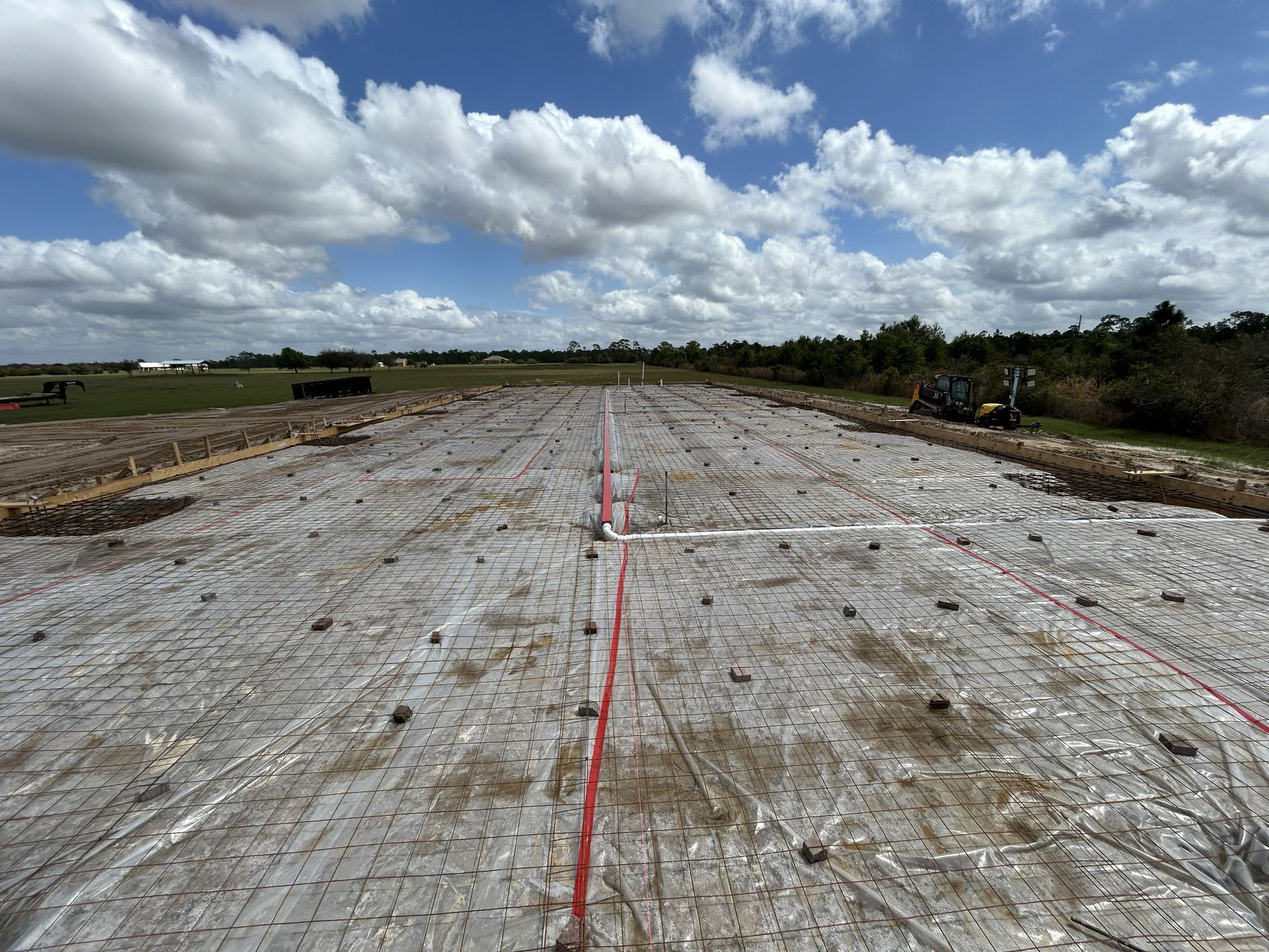 Wide gravel lot under construction with red survey line and cloudy sky
