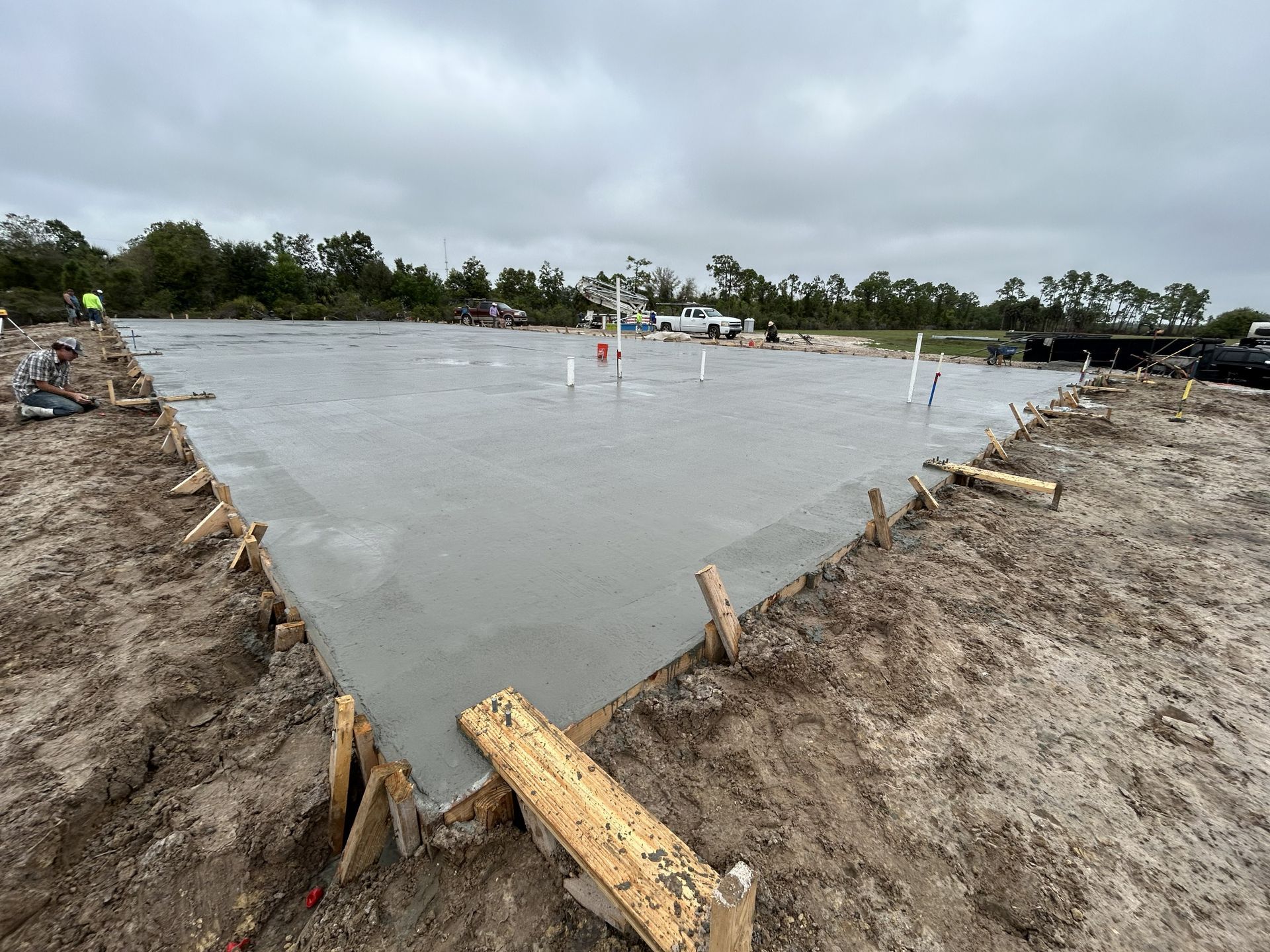 Concrete foundation slab under construction on a muddy site with wooden formwork and cloudy sky