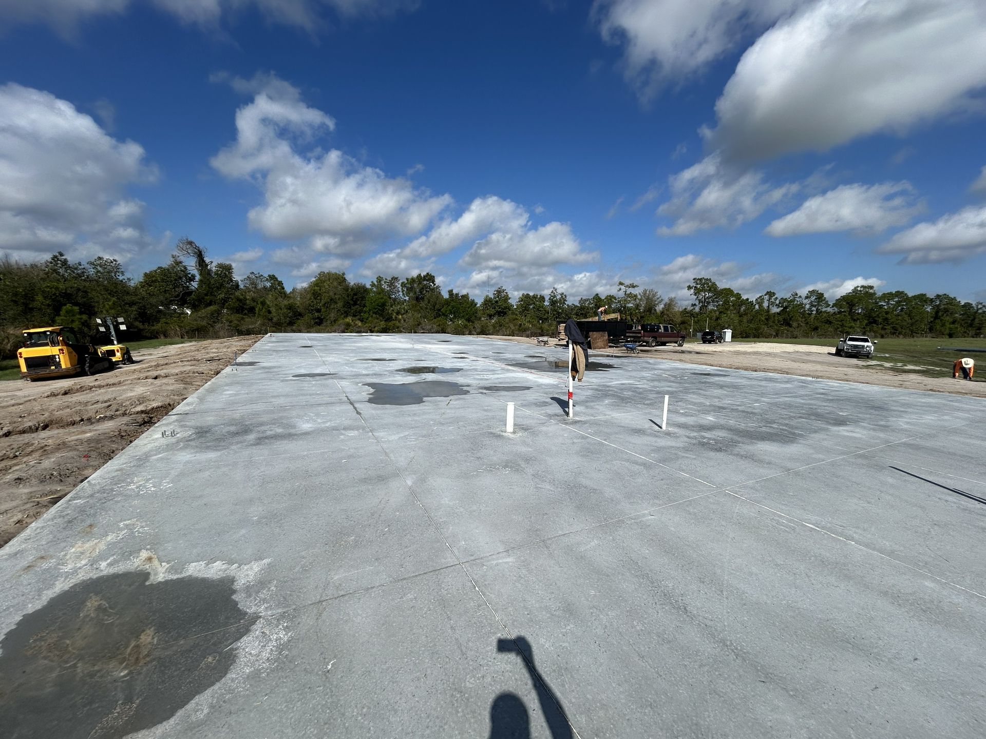 Large concrete slab under construction with workers, machinery, and a blue sky with clouds