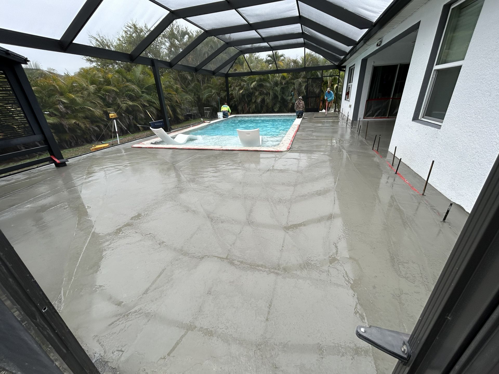 Covered patio with wet concrete beside a swimming pool and screened enclosure
