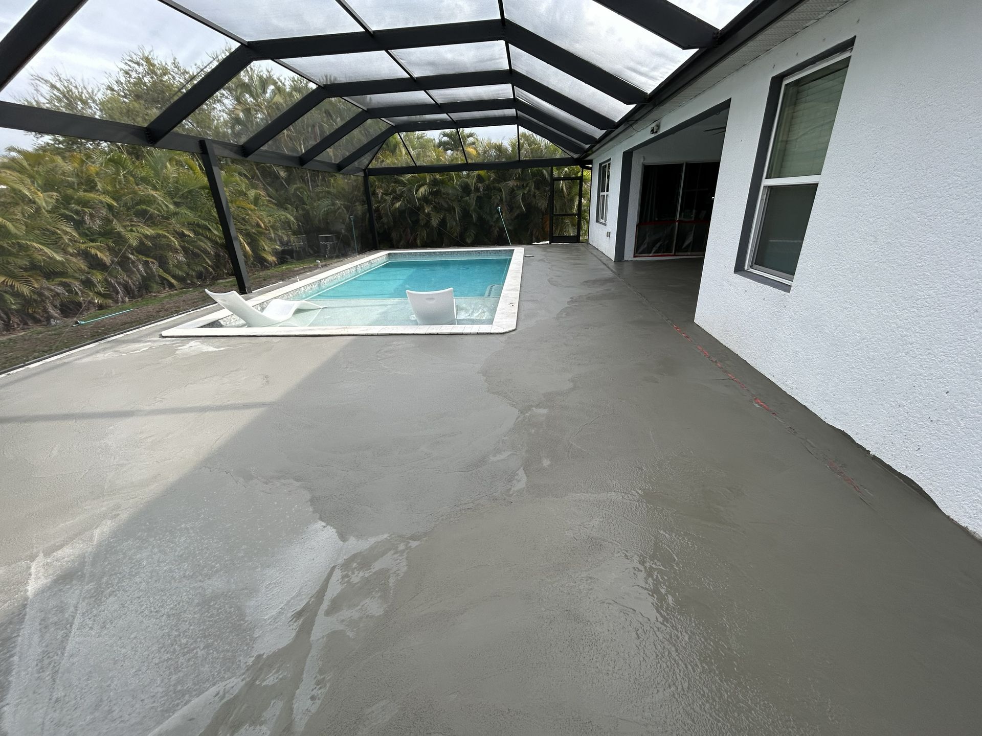 Screened patio beside a pool, with wet concrete floor and white house exterior.