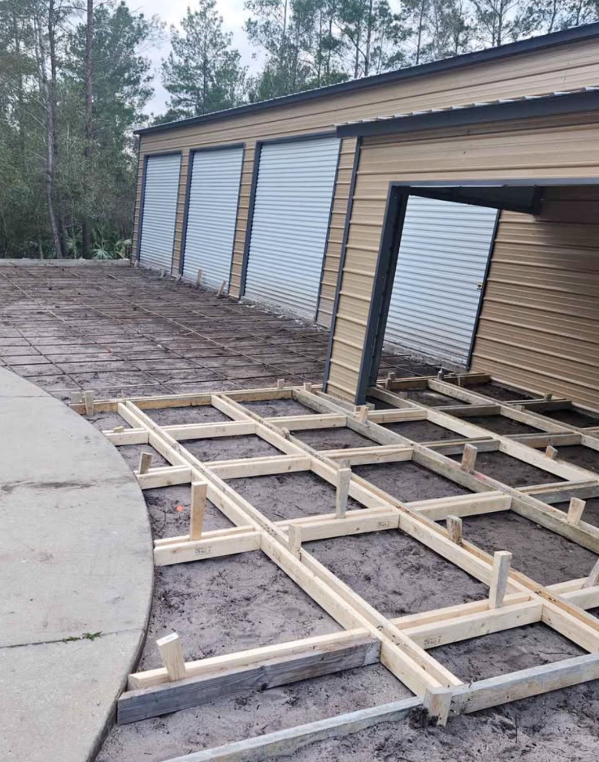 Wooden framing laid over a driveway beside a row of garage doors under construction.