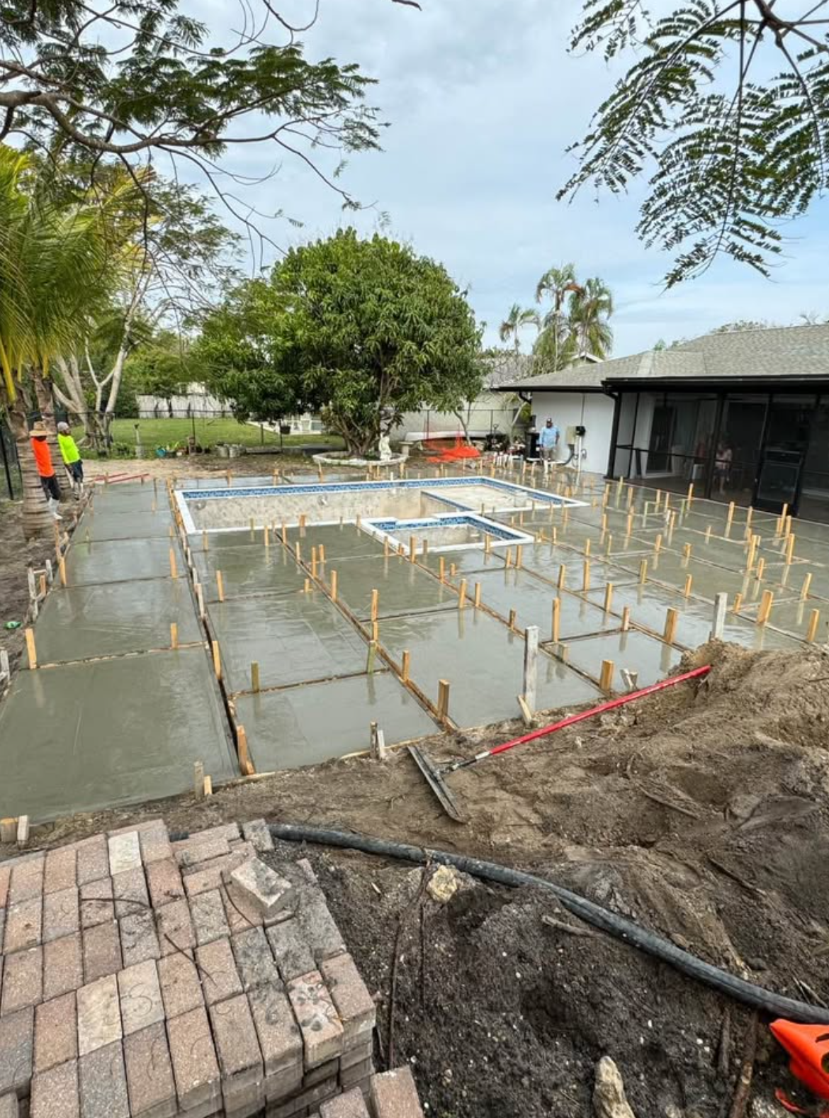 Concrete slab construction site with rebar stakes, workers, and a building in the background