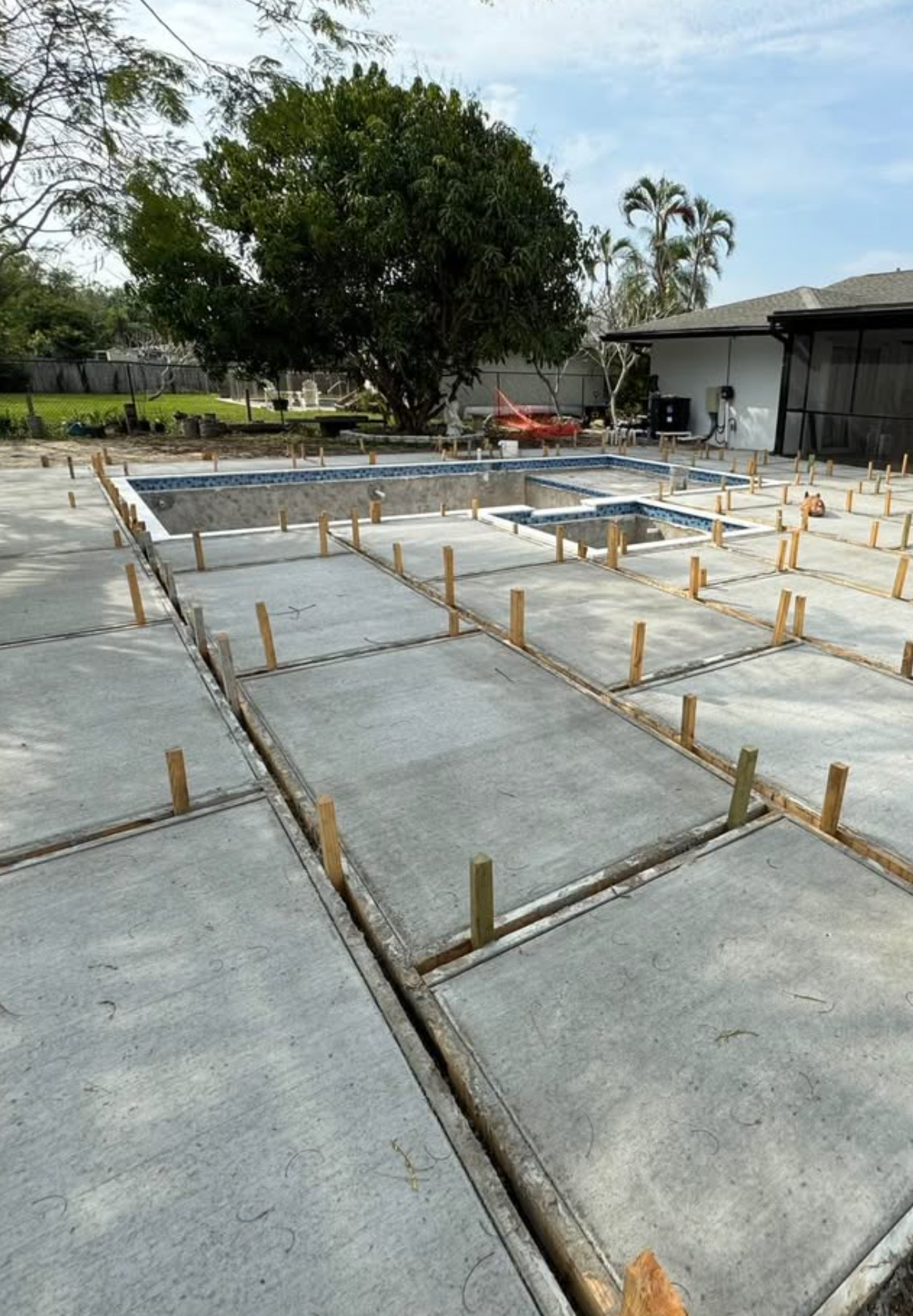Concrete foundation forms with wooden stakes in an outdoor construction site, with trees and a shed nearby