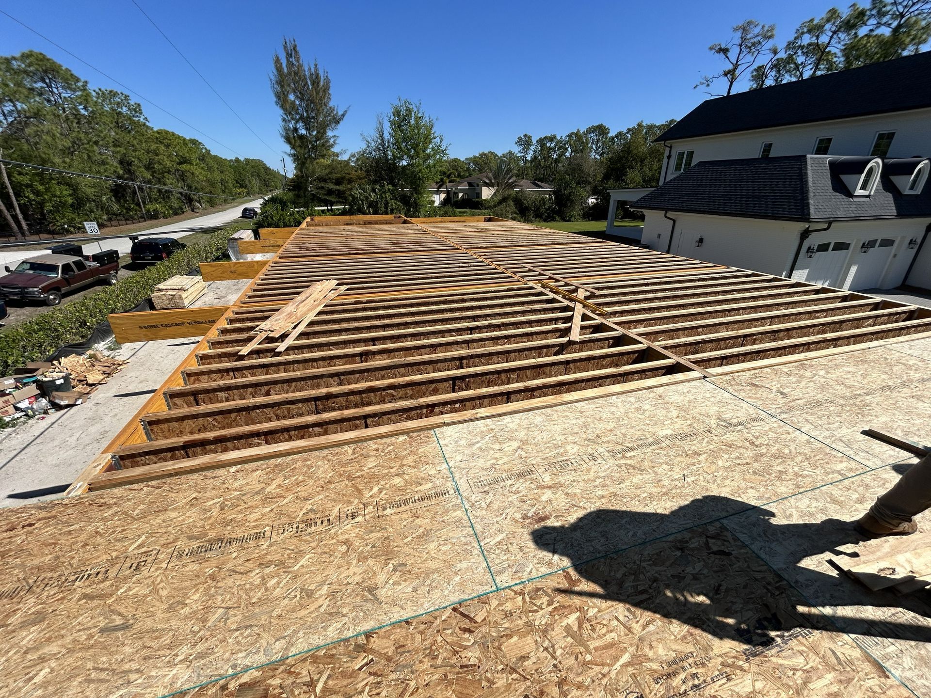 Roof framing under construction on a house, with exposed wooden trusses and a worker’s shadow in foreground.
