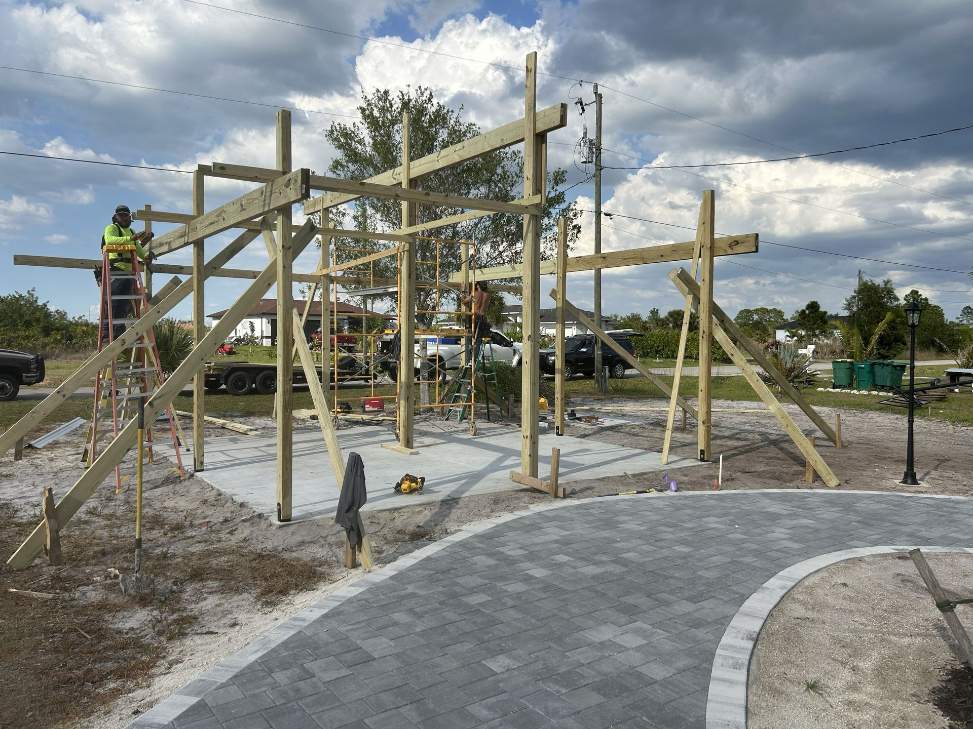 Wooden playground structure under construction beside a curved paved path, with cloudy sky overhead.