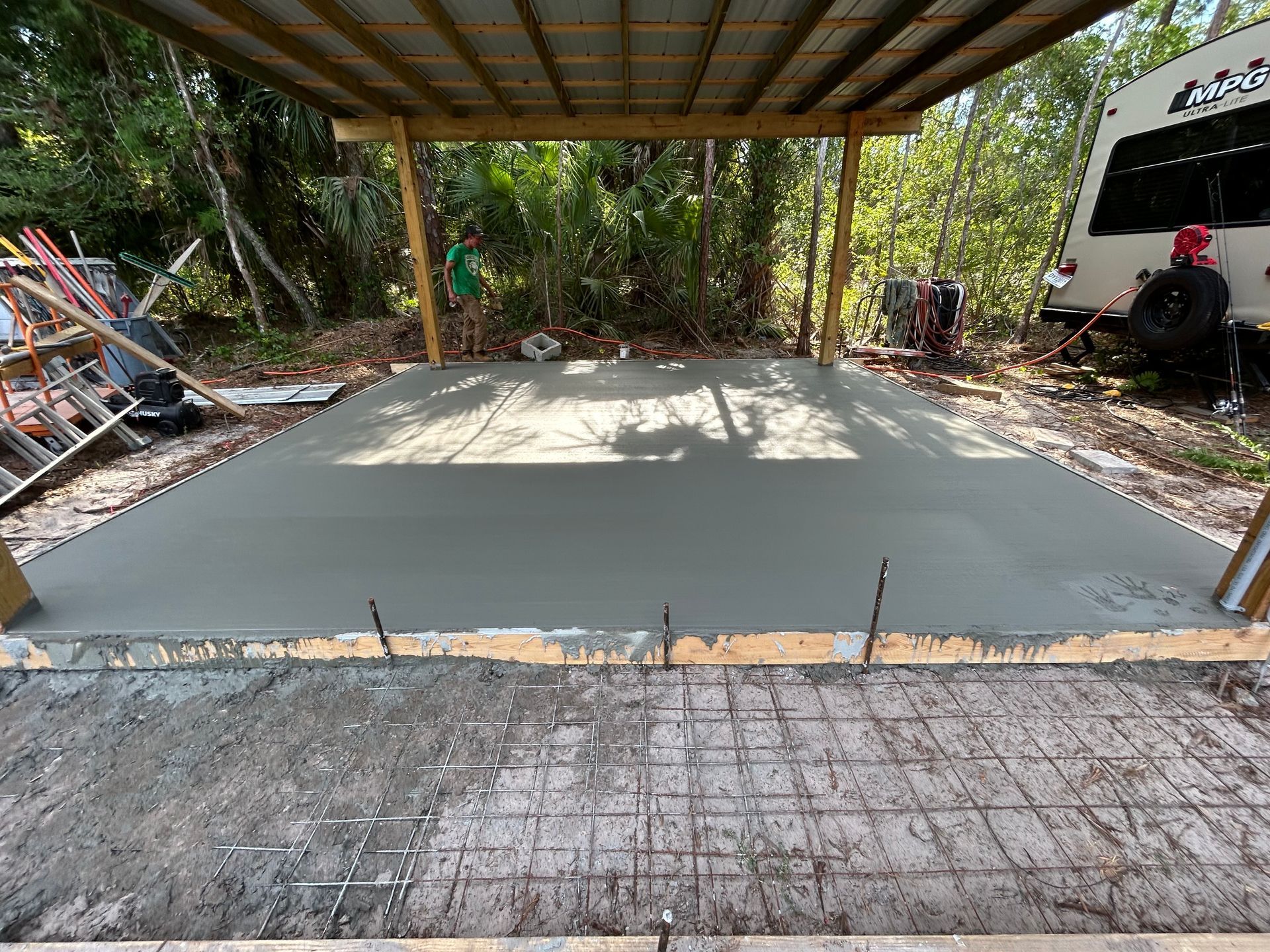 Fresh concrete slab under a roofed outdoor structure with construction materials nearby