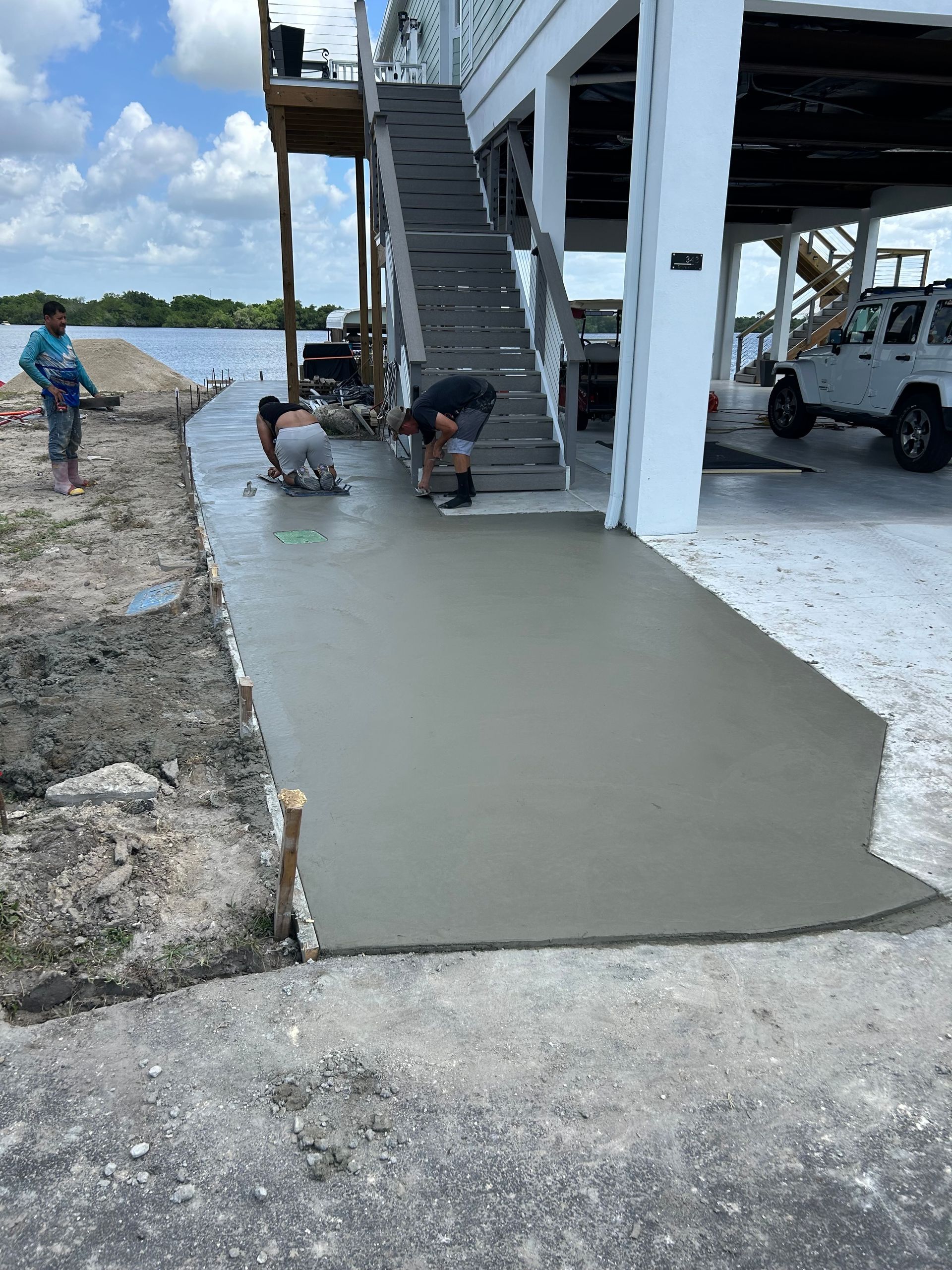 Workers smoothing fresh concrete ramp beside a raised building under construction