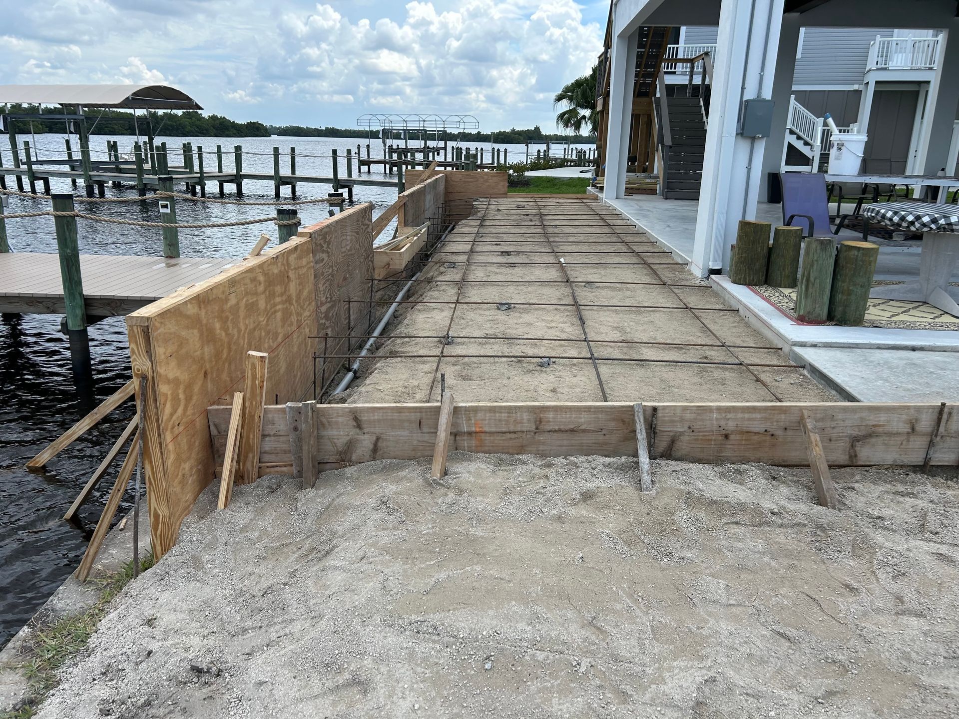 Partially built waterfront walkway with plywood barriers and dock pilings beside a marina