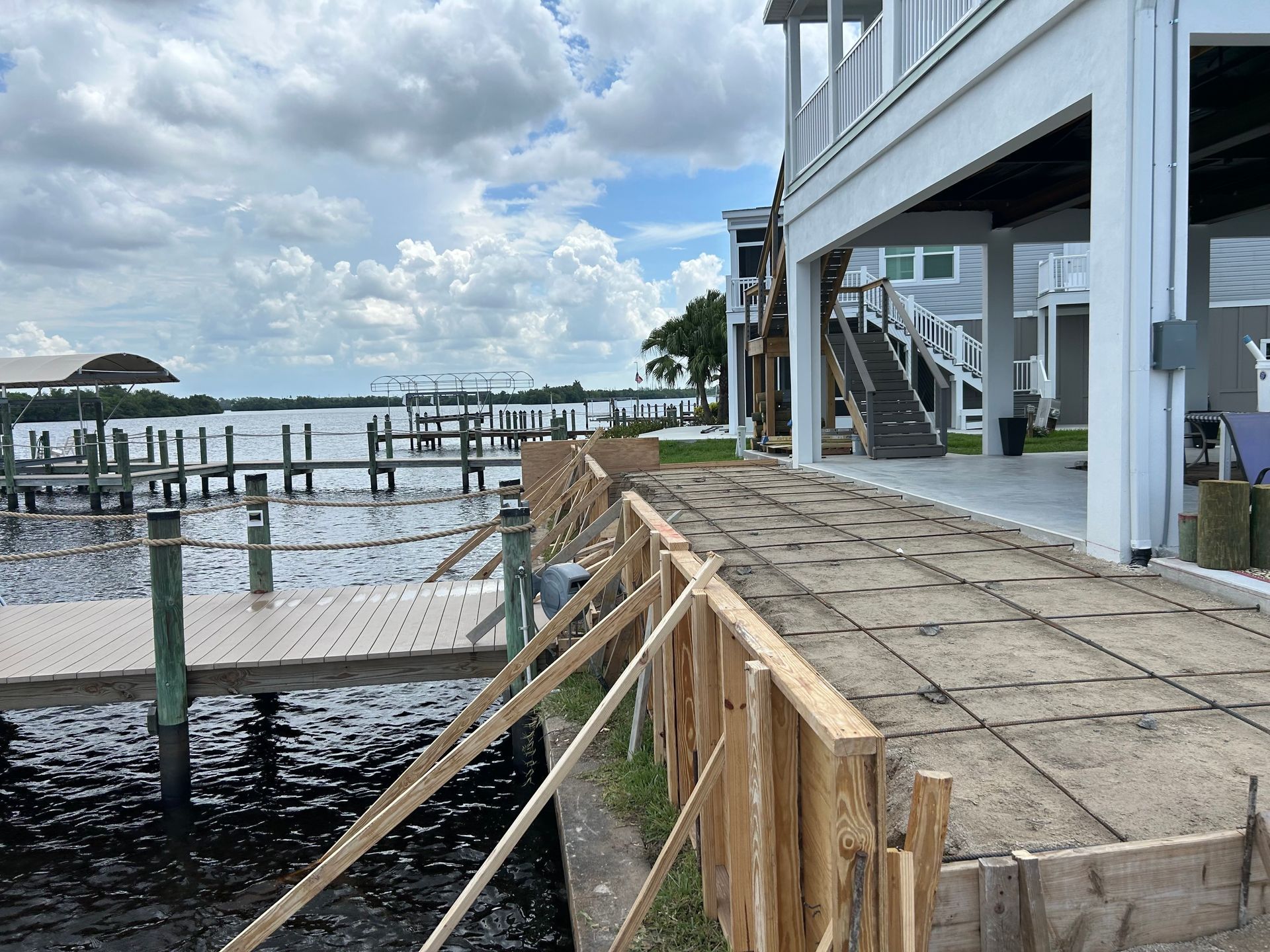 Deteriorating waterfront dock beside a building, with broken wooden railing and pilings over water under cloudy skies