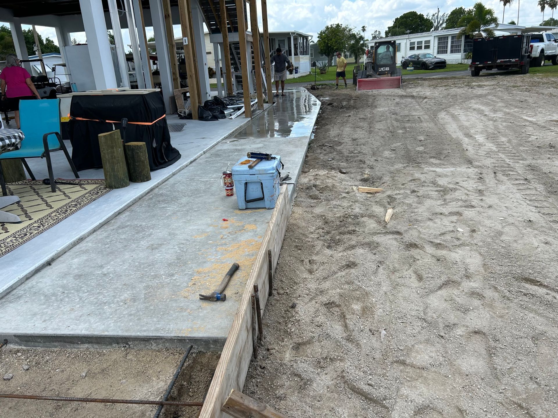 Concrete walkway under construction beside dirt lot, with tools and building materials along the edge.