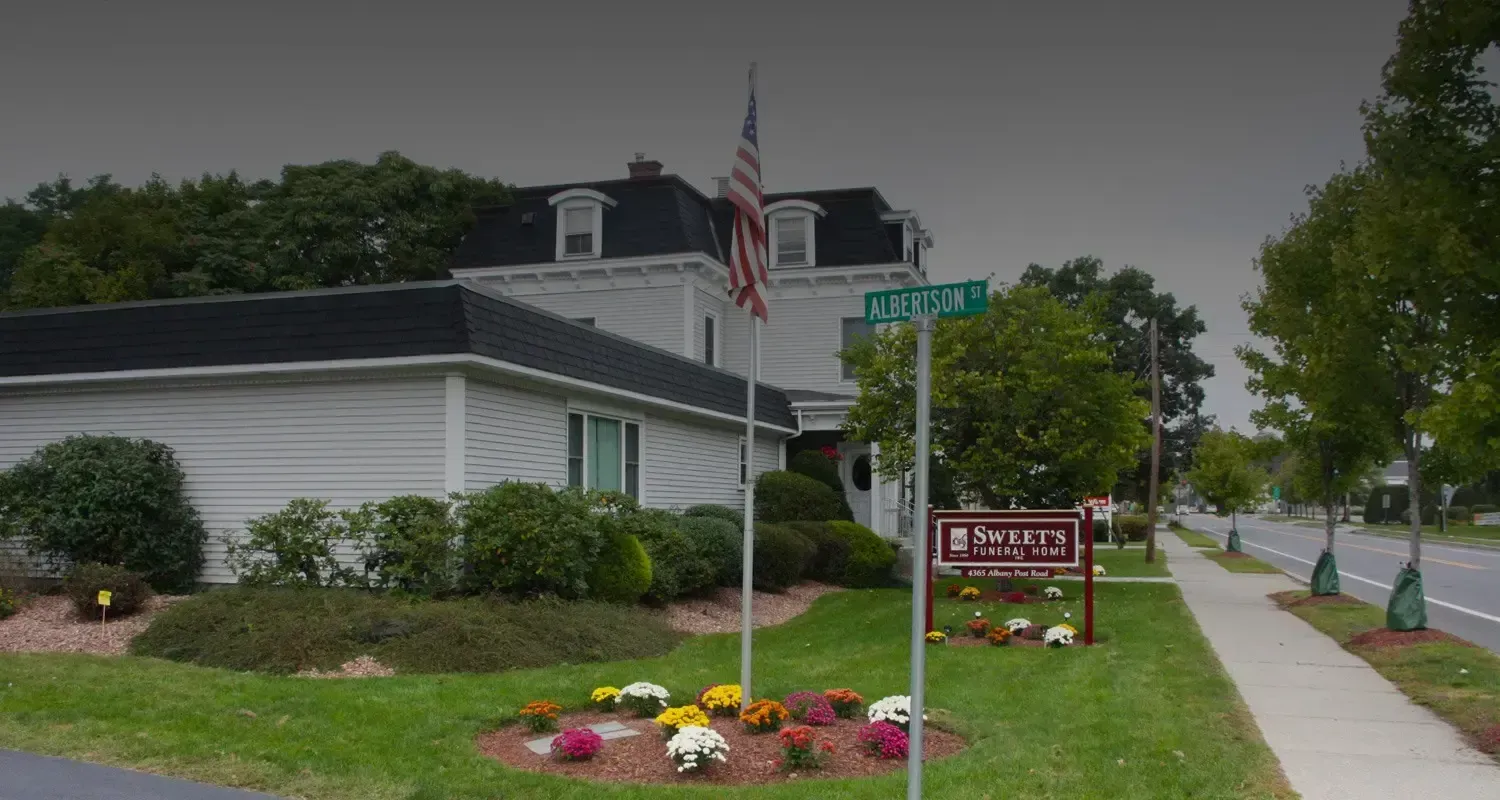 Building with sign for funeral home, American flag, flowers, green lawn, and street.
