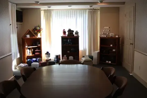 A room with an oval table surrounded by chairs, three bookcases, and a window with curtains.