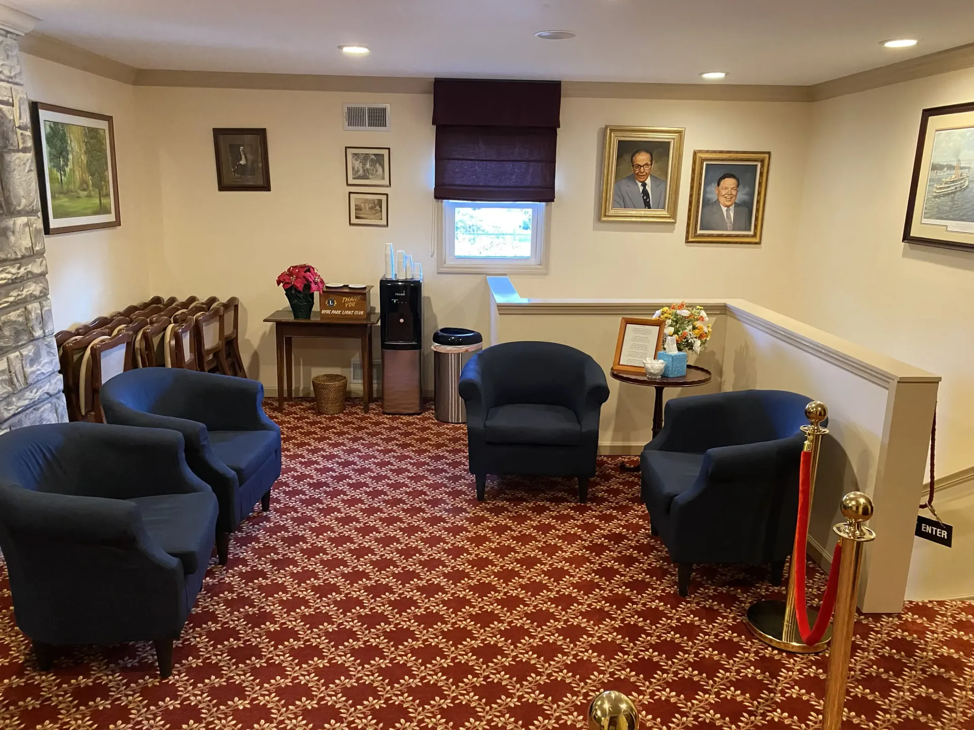 A waiting area with four blue chairs, portraits, and a red patterned carpet.