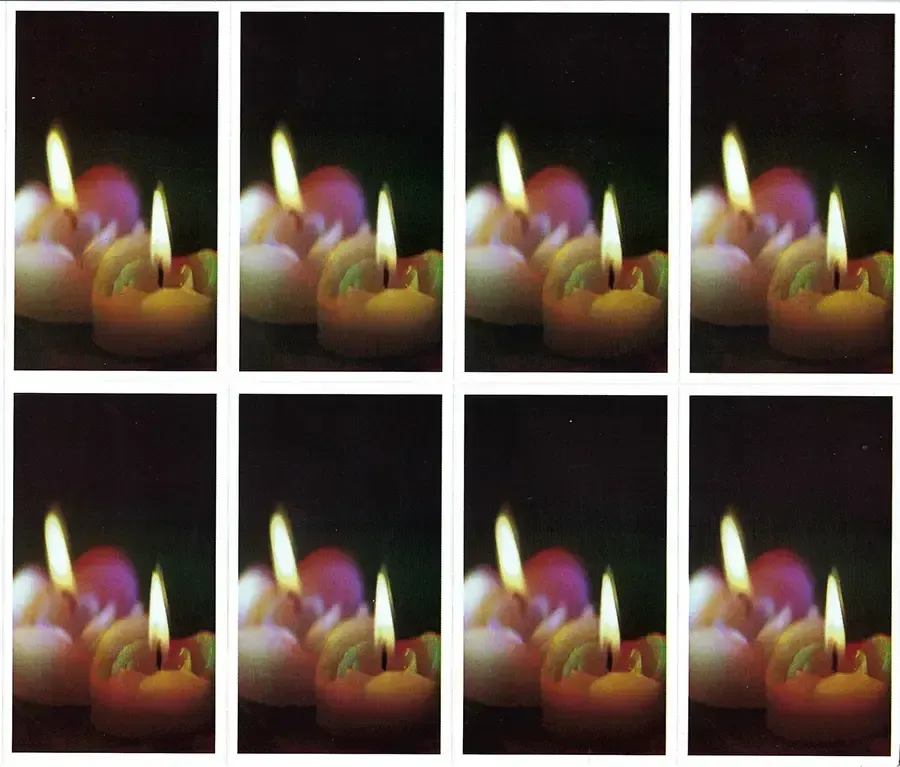 Prayer Cards-- Eight small candles burning, with orange and purple flames against a dark background.