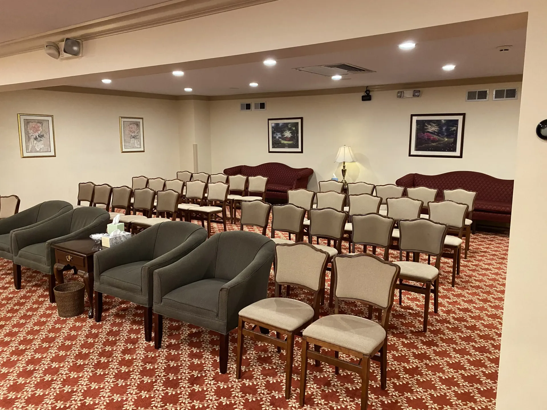 A conference room with rows of chairs and sofas, a red patterned carpet, and artwork on the walls.